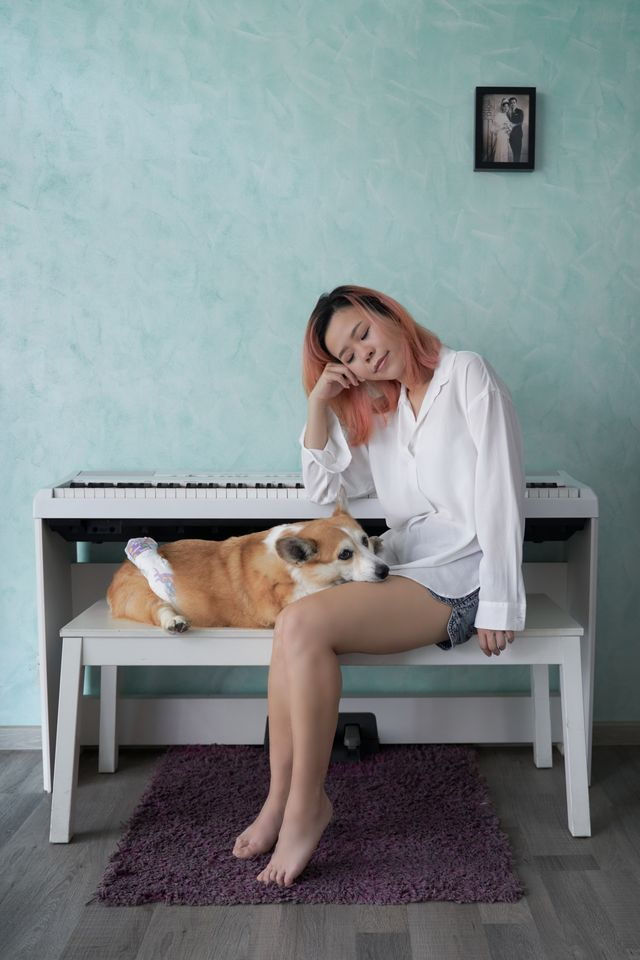 An owner resting beside her corgi on a piano bench