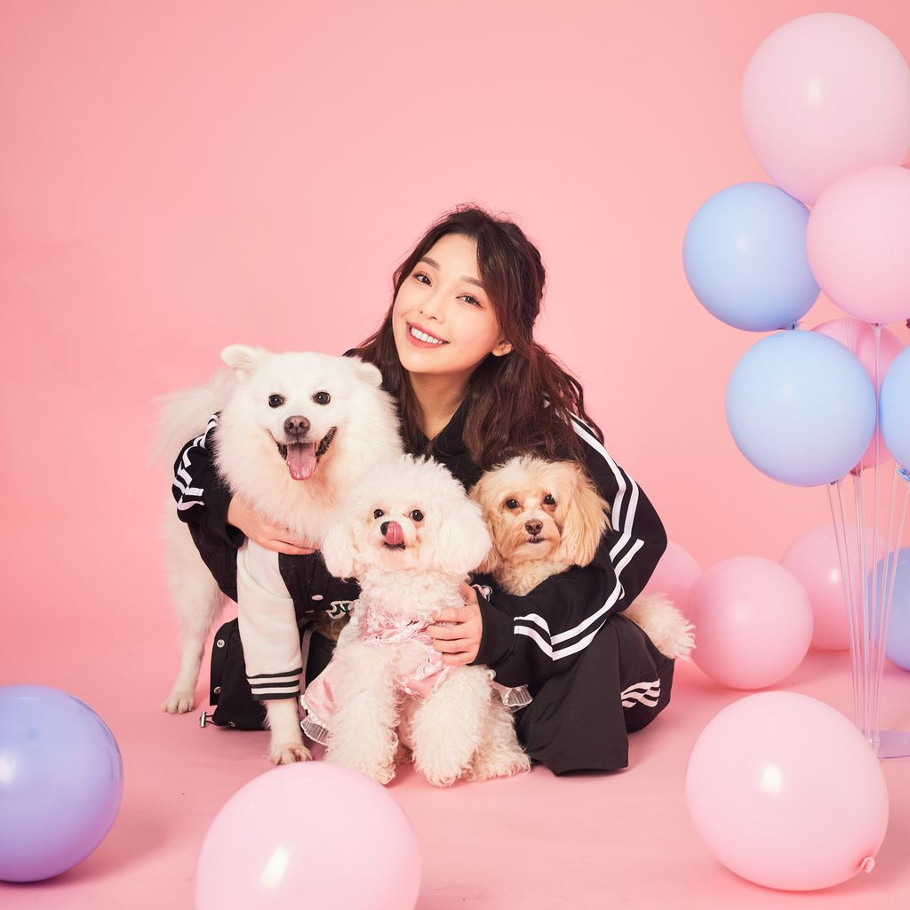 An owner with three small dogs among pink and blue balloons