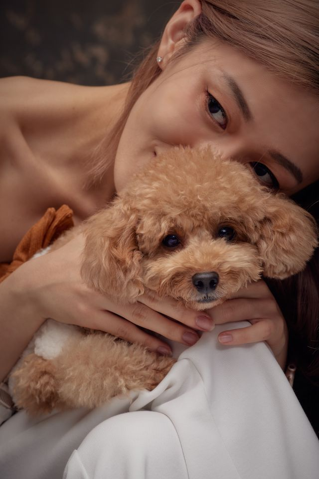 An owner cuddling her toy poodle cheek to cheek